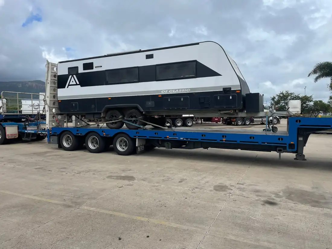 Family caravan chained down on a low-loader trailer, heading to the terminal